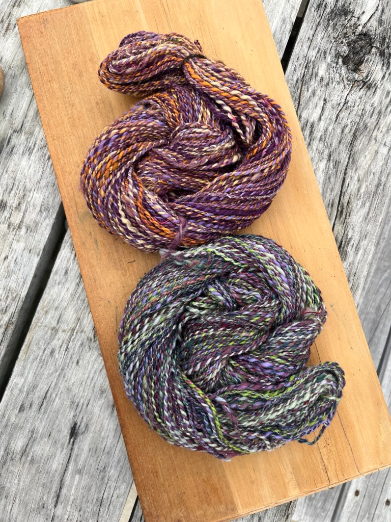 Vibrant purple and orange NZ wool handspun yarn, blended on Ashford drum carder, eco-friendly fiber for handmade crafts, light wood backdrop.