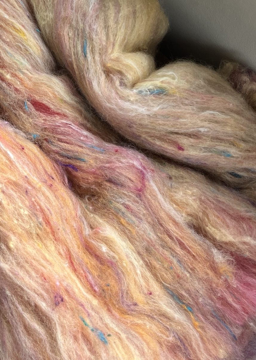 Handmade wool batt for spinning or felting: bright yellow NZ wool blended with sari silk, mulberry silk and kid mohair, featuring yellow and white accents, curled into a spiral on a natural wood background.