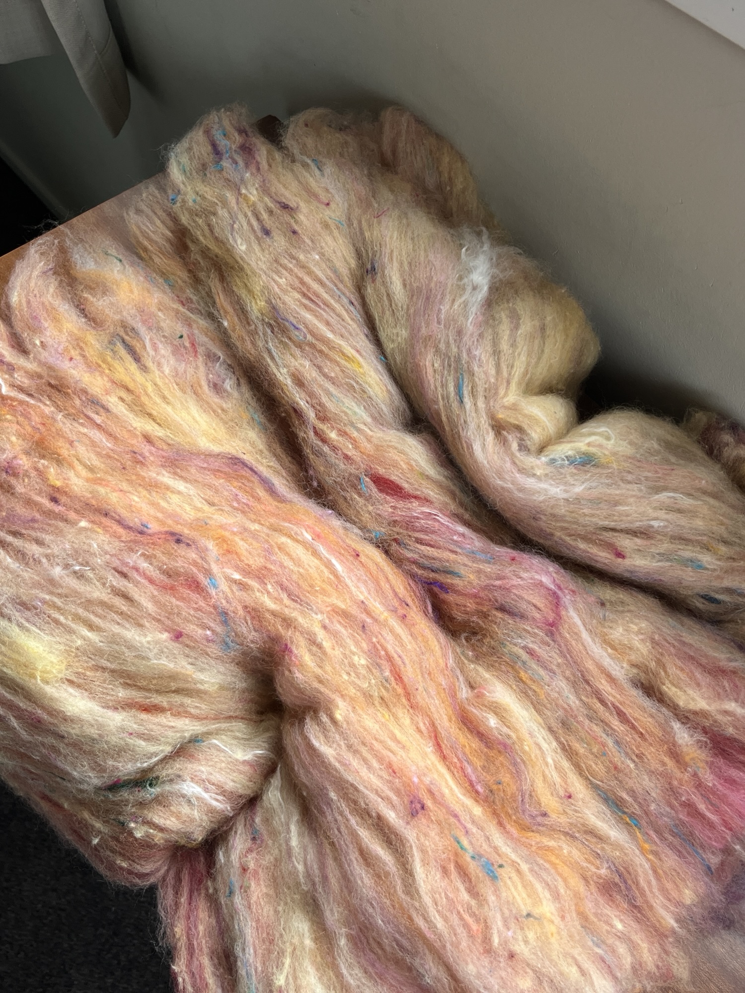 Handmade wool batt for spinning or felting: bright yellow NZ wool blended with sari silk, mulberry silk and kid mohair, featuring yellow and white accents, curled into a spiral on a natural wood background.