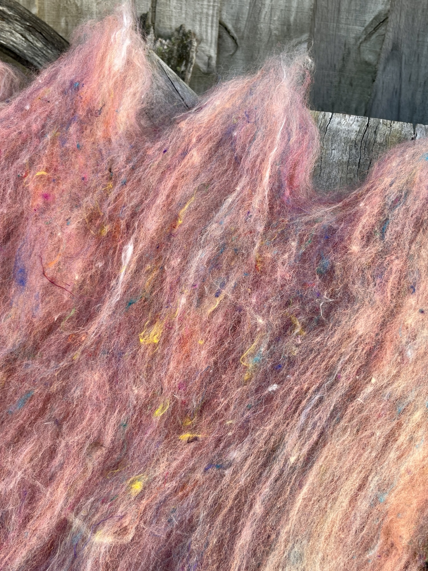 Handmade wool batt for spinning or felting: bright orange and yellow NZ wool blended with sari silk, mulberry silk and kid mohair, featuring yellow and white accents, curled into a spiral on a natural wood background.