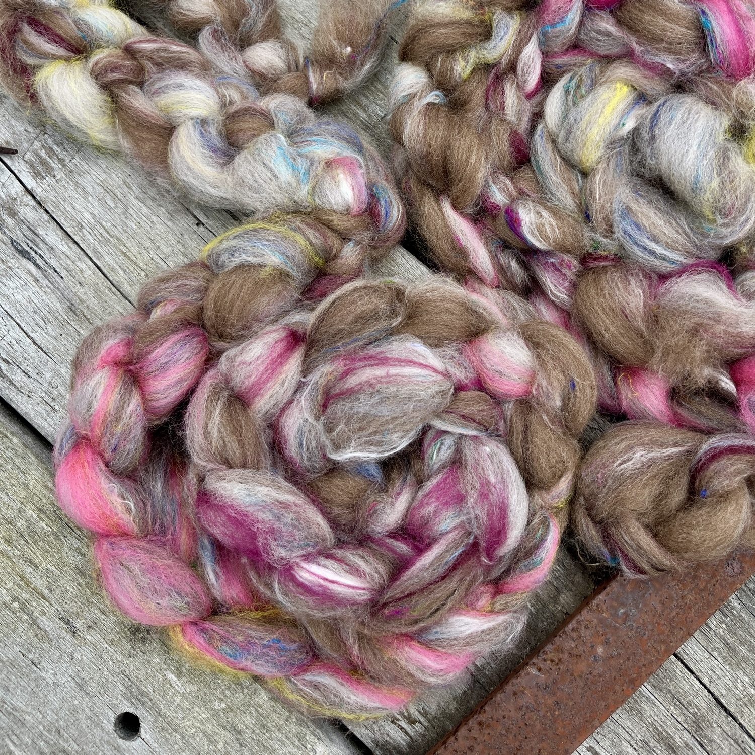Caramel toffee colored Haunui natural undyed wool with lashings of Ashford spinning fibre in bright pinks and some dashes of yellow, blue and undyed white wool. The fibre isplaited into a braid, a common fiber prep for selling wool to handspinners and felters