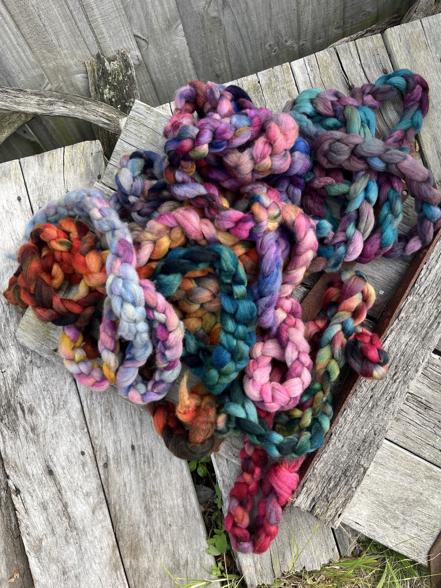 Braids of bright coloured roving for spinning and felting are tossed in a pile on a light slatted wood background